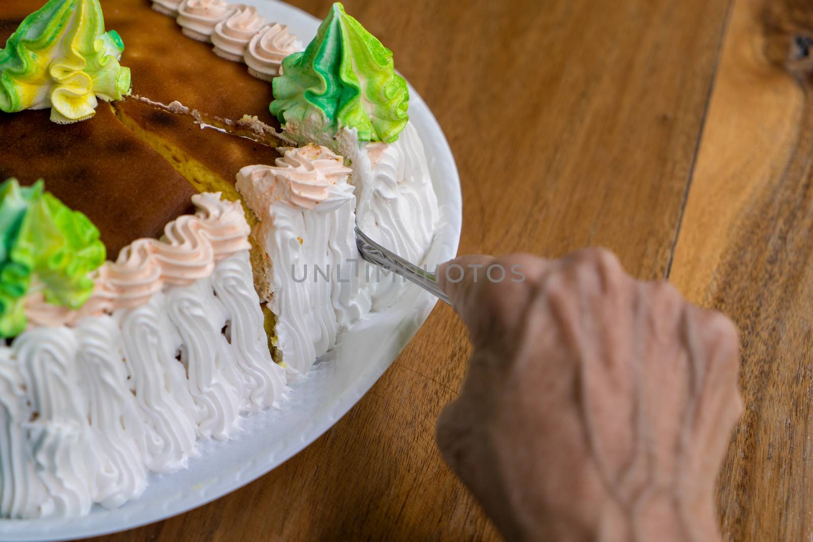 A closeup of a cake and an wrinkled old hand cutting the cake