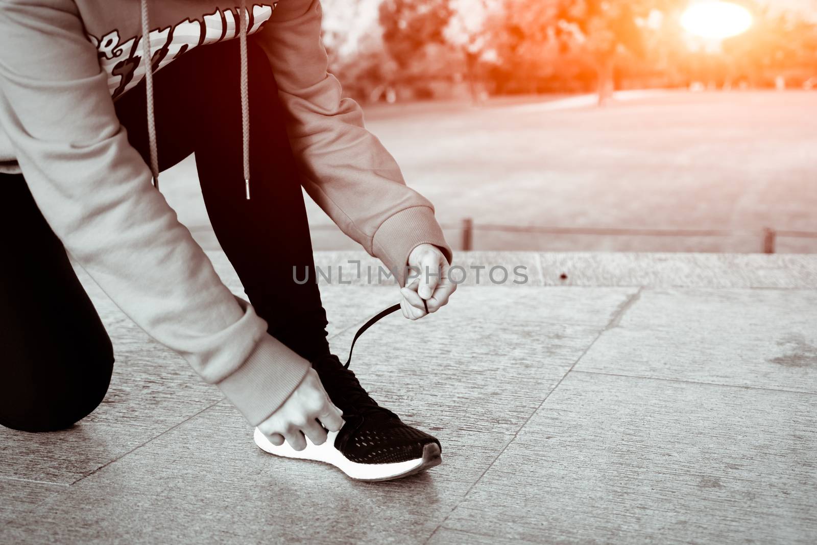 close up young woman tying shoelace while walking, sunny day in winter season- B&W filter