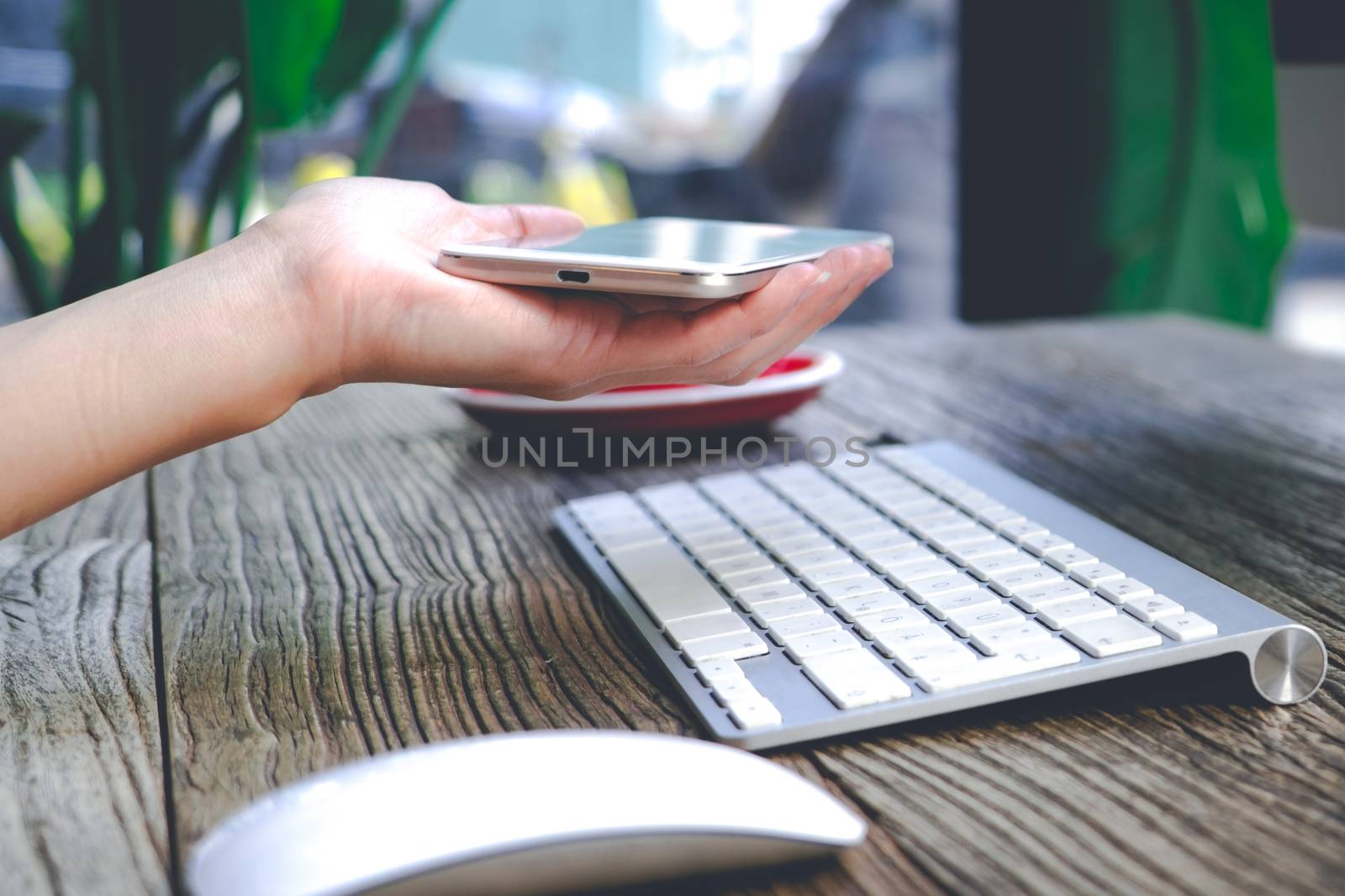 the woman hand holding the smart mobile phone with the keyboard and mouse