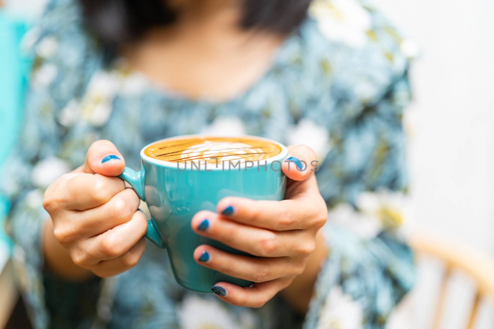 Latte art coffee cup in green glass on women hand