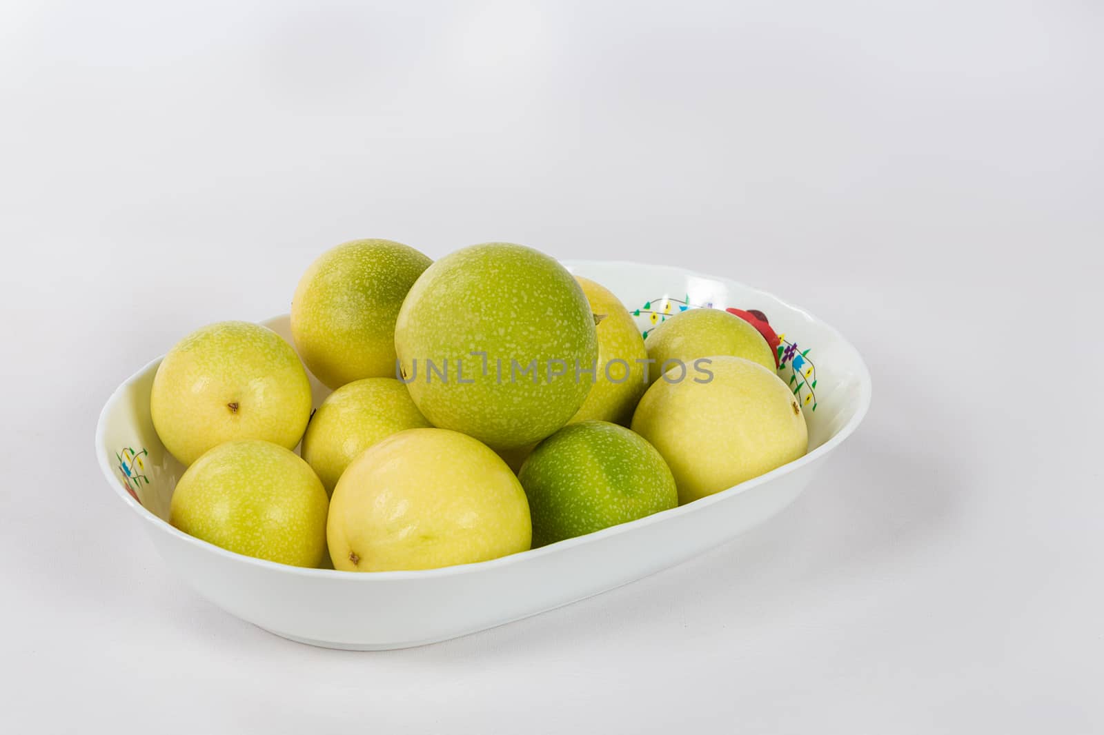 A group of ten passion fruit in a bowl on a white background