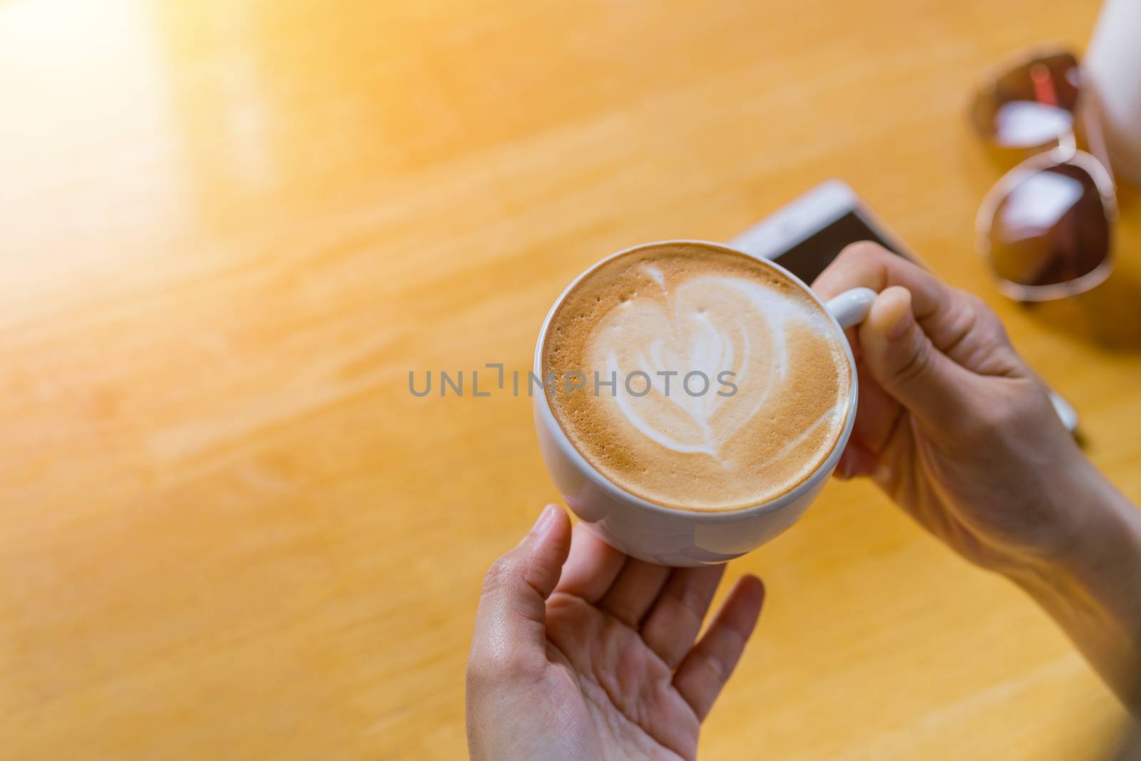 women hands holding hot cup of coffee or tea in morning sunlight