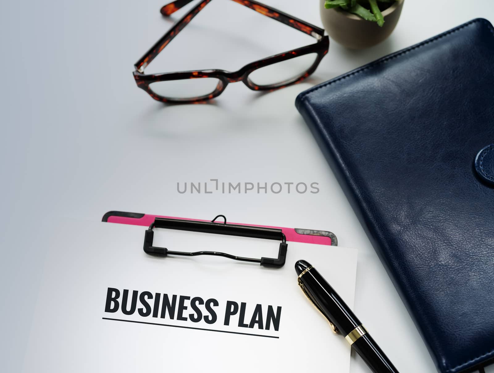 Business plan concept, pen and clipboard with word Business plan, glasses and diary book on white background with copy space