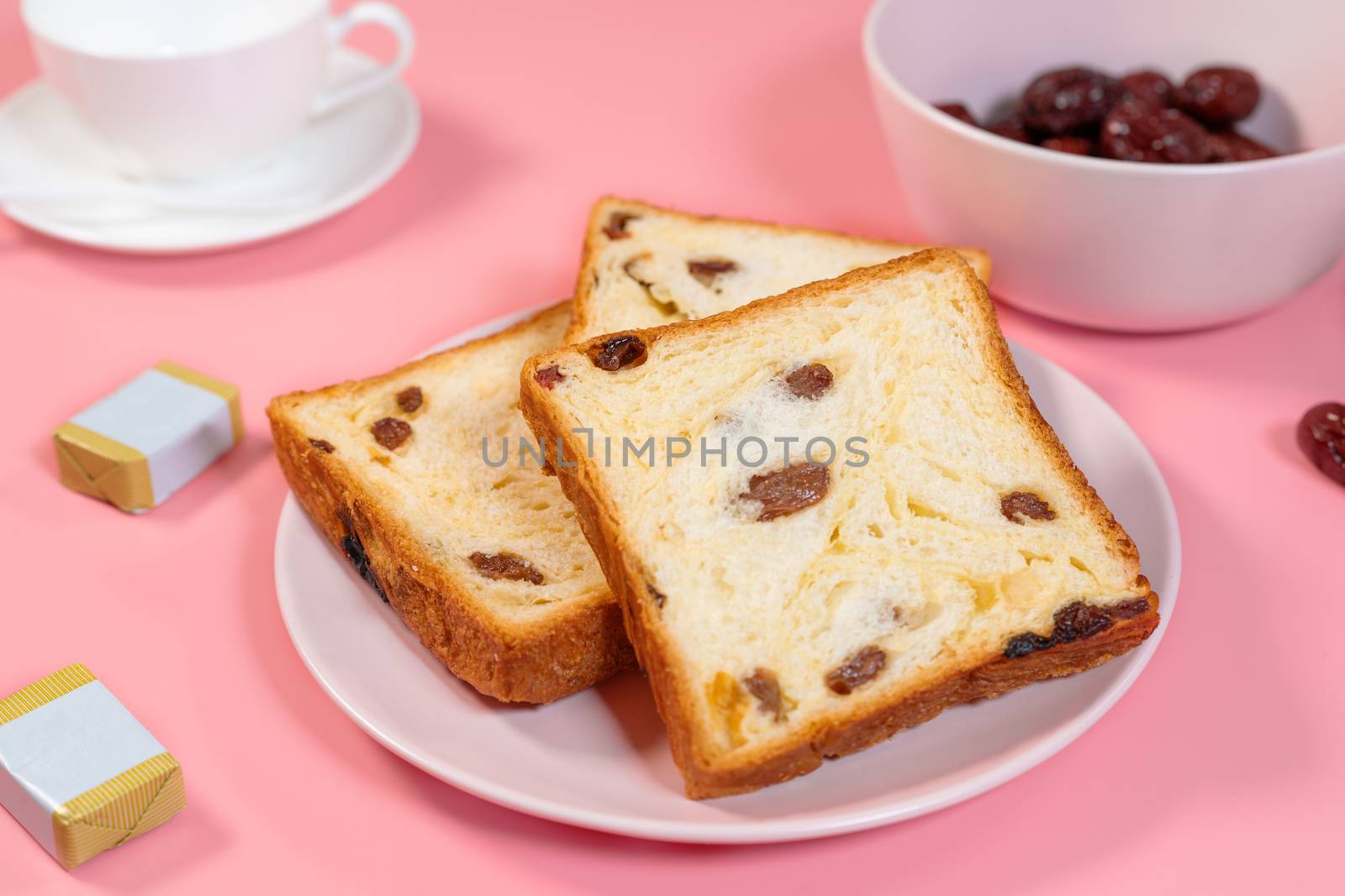 Raisin toast, butter and tea cup placed on pink table