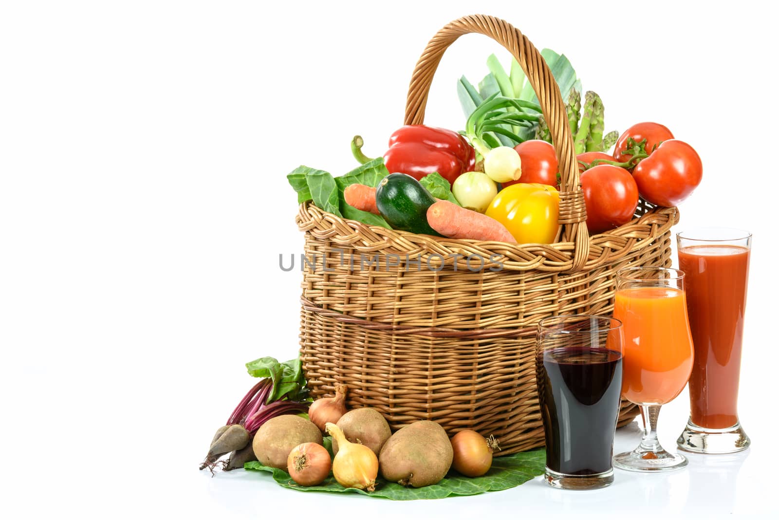 Healthy eating concept - basket full of varied vegetables and various vegetable juices in glasses on white background