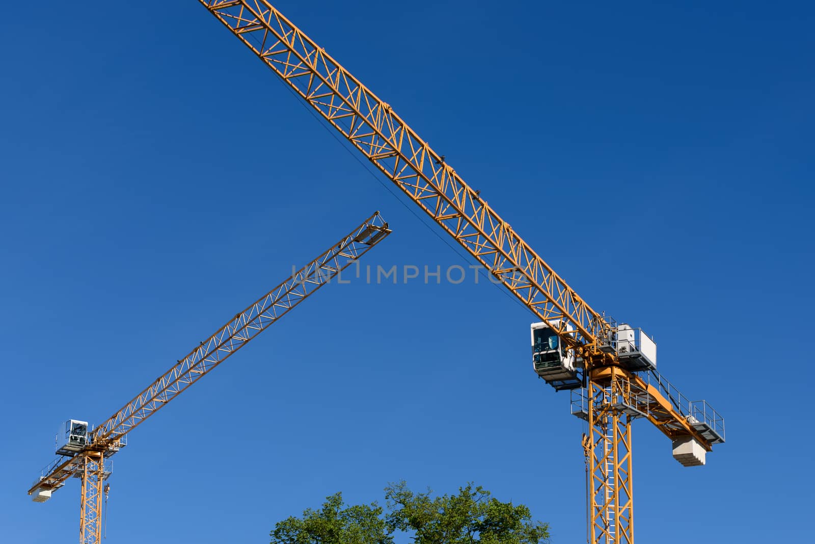 Two generic construction cranes on a blue sky background.