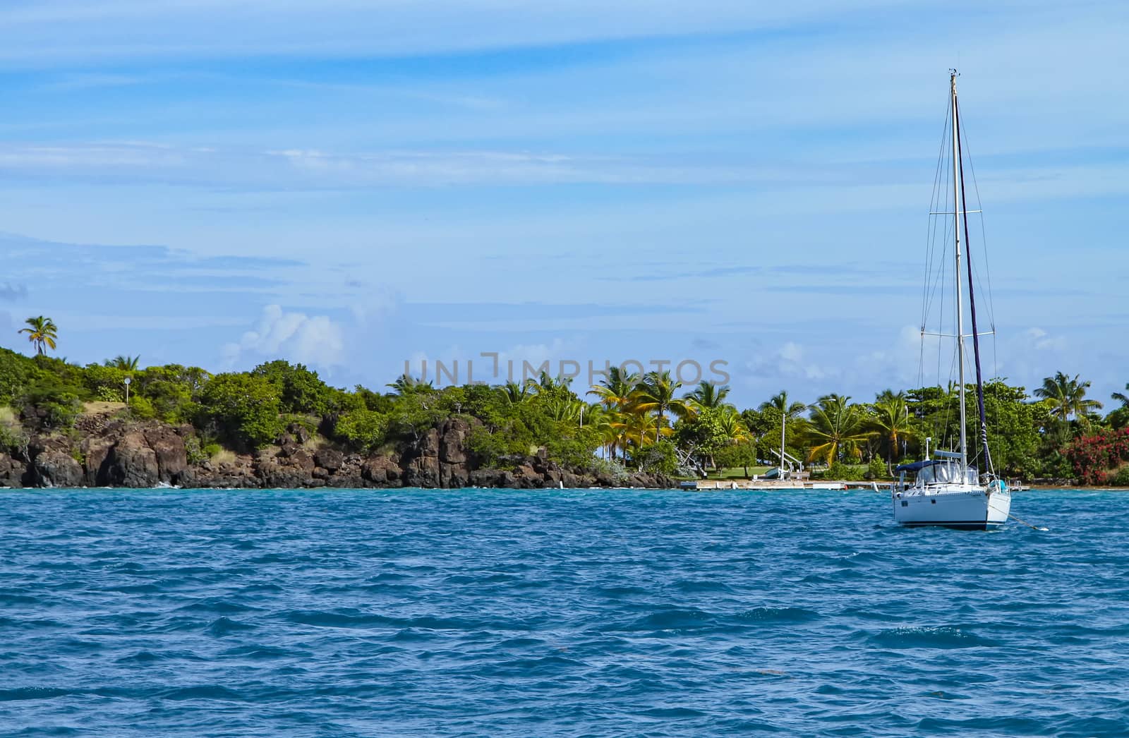 A small white sail boat anchored near the coast of a Puerto Rican island.