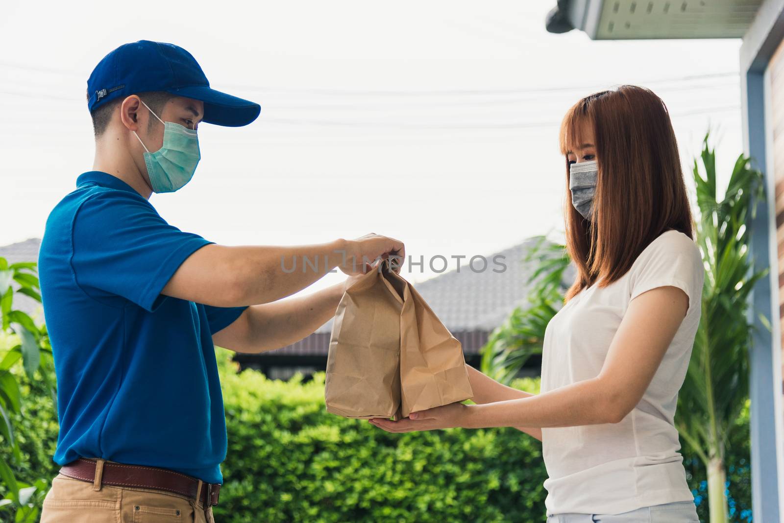 Asian delivery express courier young man giving paper bags fast food to woman customer receiving both protective face mask, under curfew quarantine pandemic coronavirus COVID-19