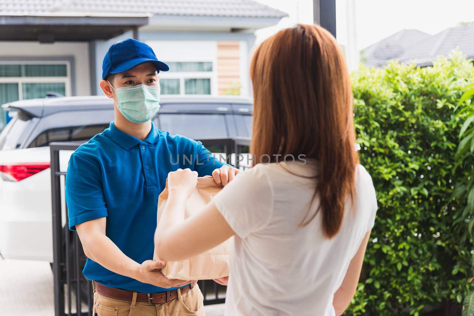 Asian delivery express courier young man giving paper bags fast food to woman customer receiving both protective face mask, under curfew quarantine pandemic coronavirus COVID-19