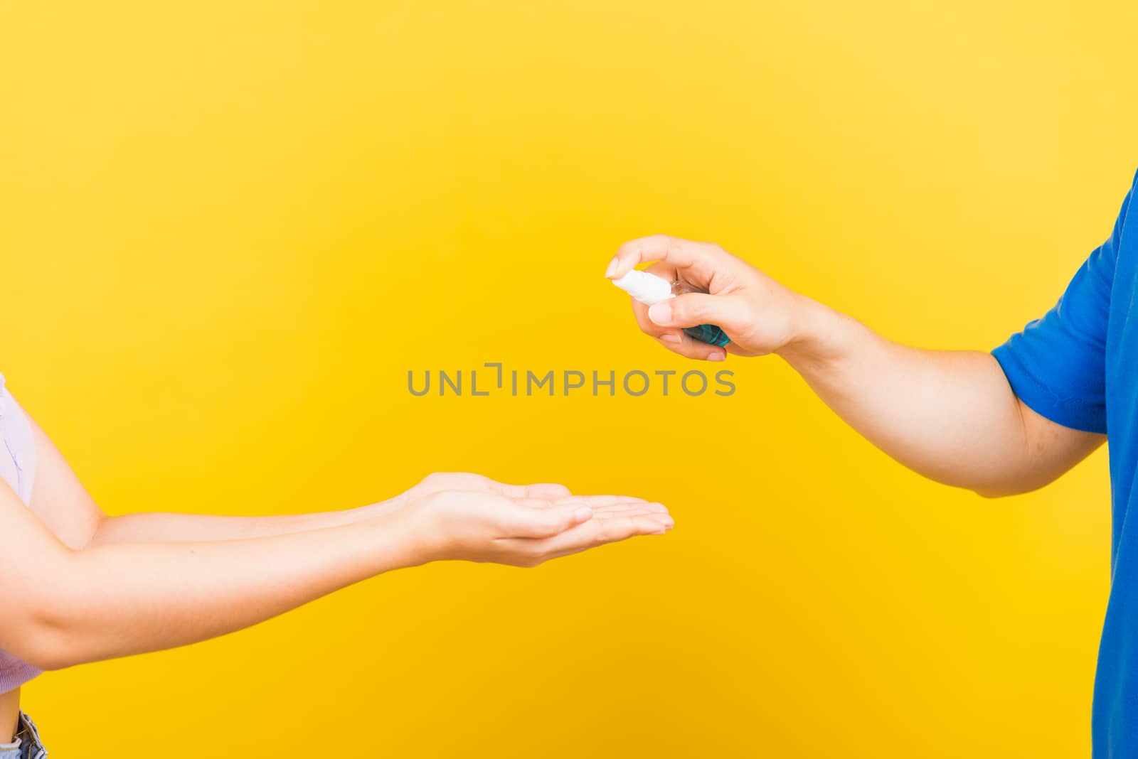 Family man applying hand spraying blue alcohol spray sanitizer clean and disinfect woman hands, Protection Covid-19 coronavirus outbreak, studio shot isolated on yellow background