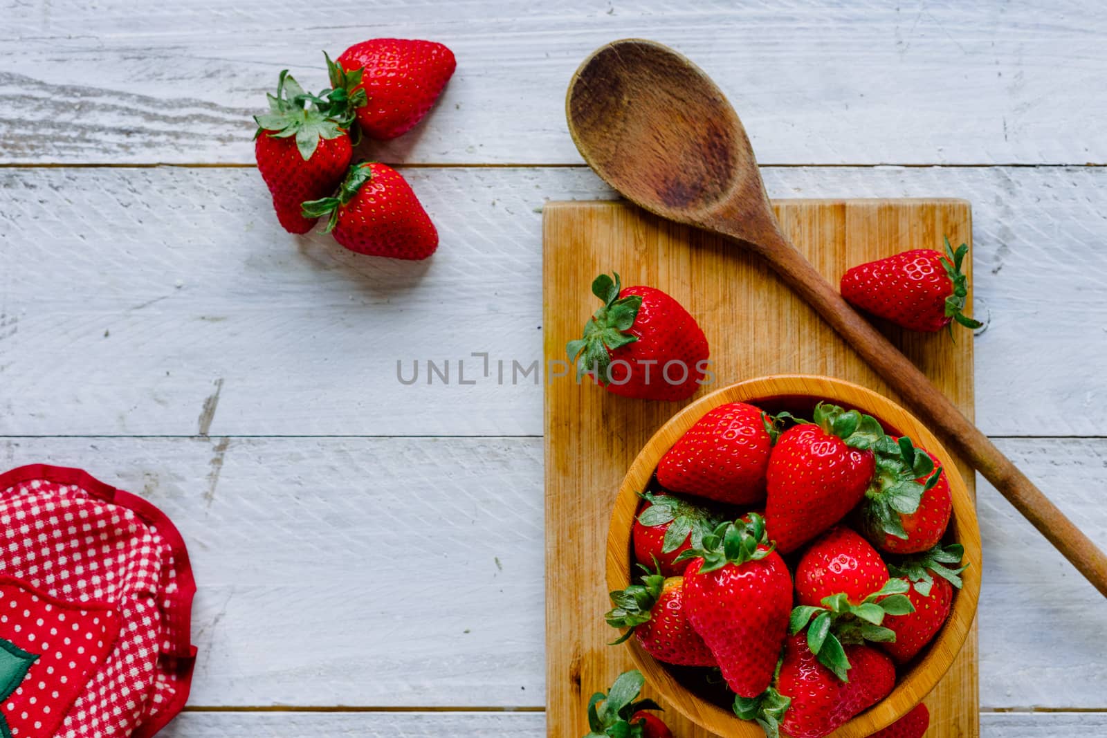 Organic strawberries on a cutting board fruit and a bowl on a white wooden table