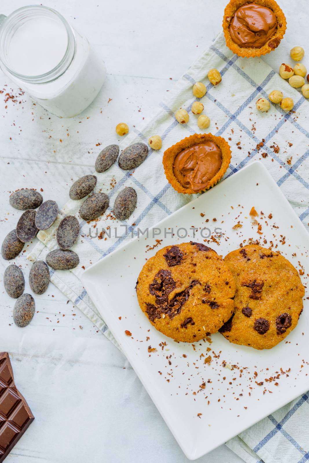 Organic chocolate chip cookies with hazelnuts, coconut milk and chocolate candies in a square plate on a wooden table