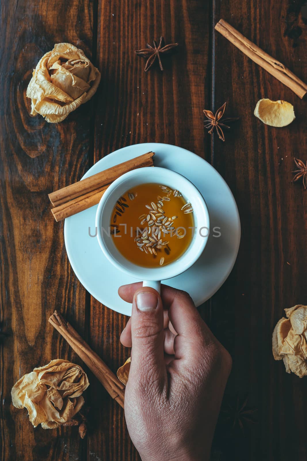 White cup of tea with one hand on a wooden table and roses around