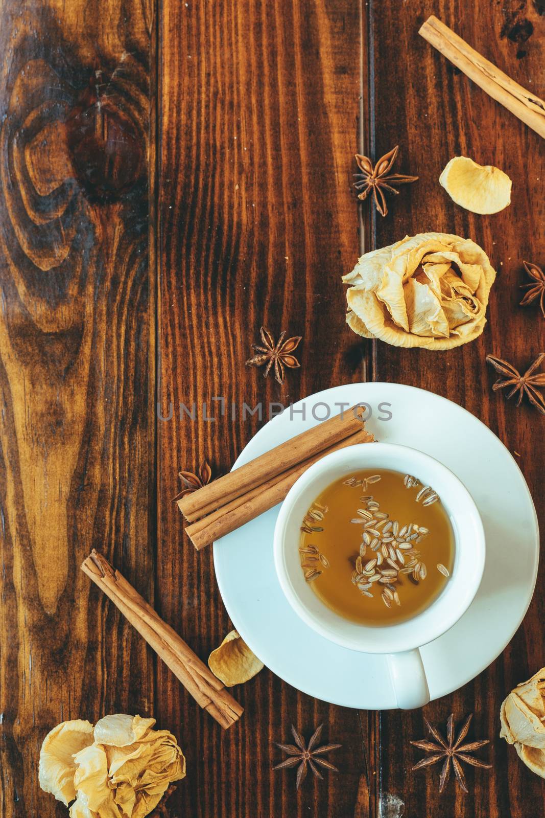 White cup of tea on a wooden table and roses and anise around
