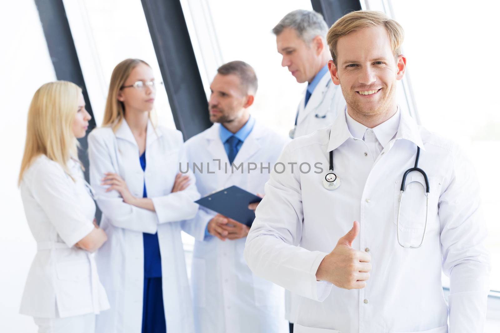 Team of medical professionals, young doctor looking at camera, smiling, showing thumb up