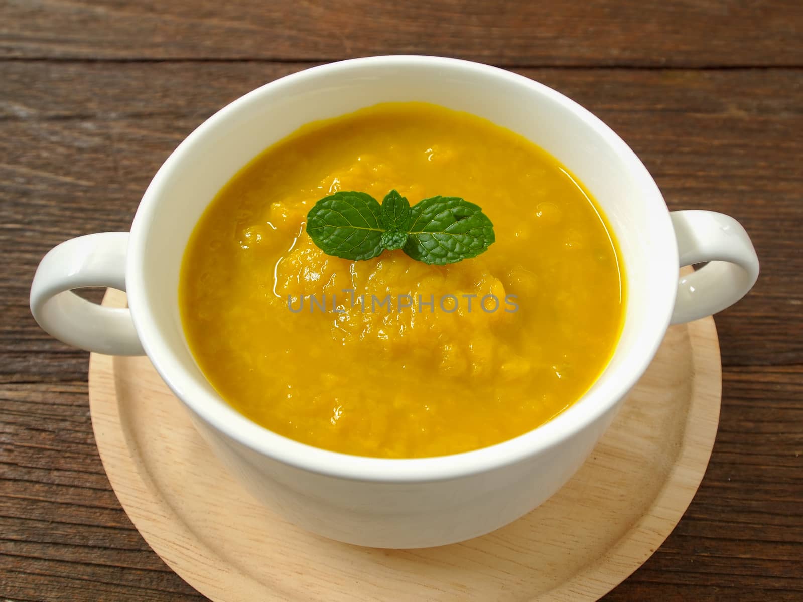 Pumpkin soup in a cup placed on a wooden table.