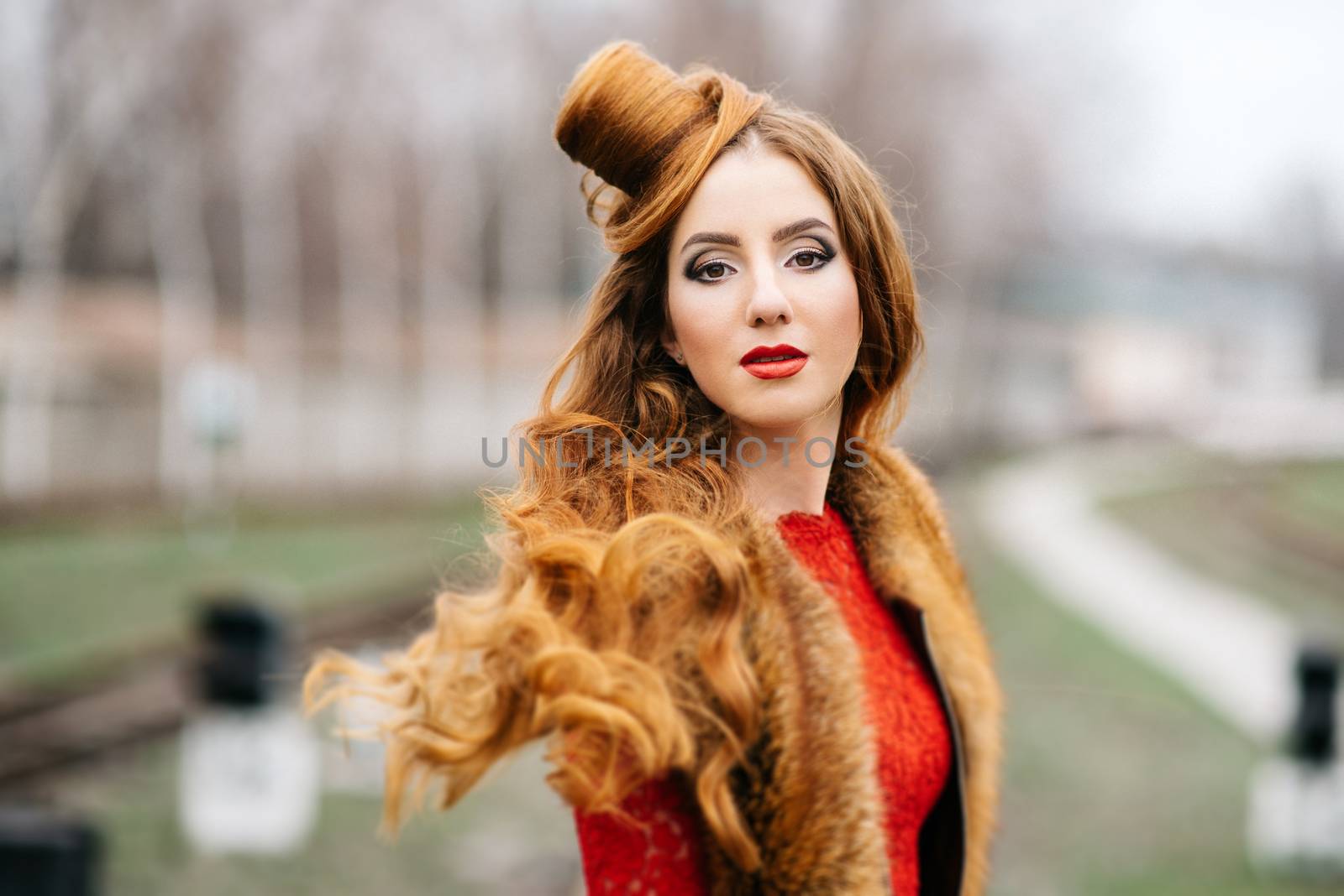 young girl with red hair in a bright red dress on the railway tracks of the station