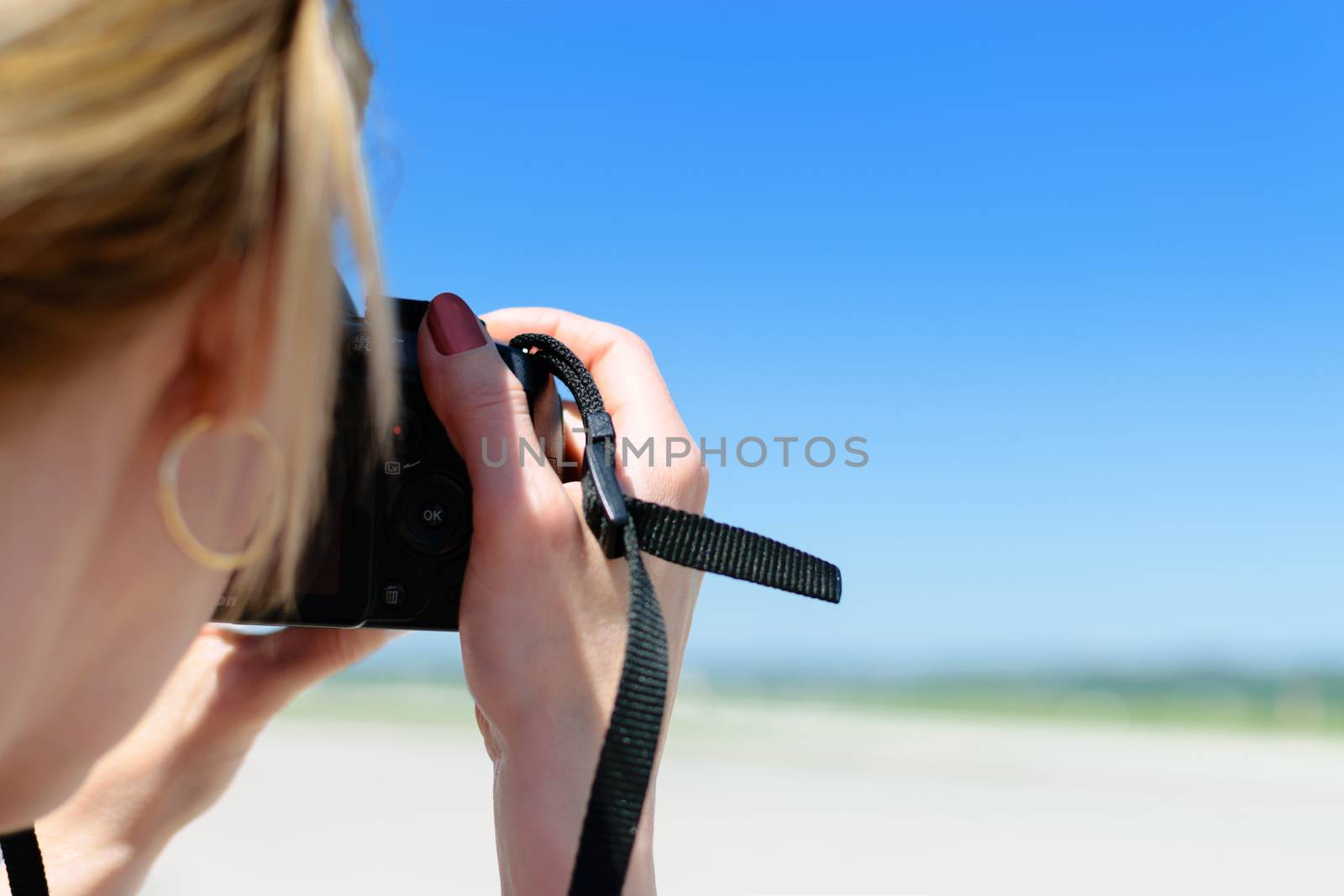 Beautiful young woman shoots a photo on the beach with a professional DSLR camera.