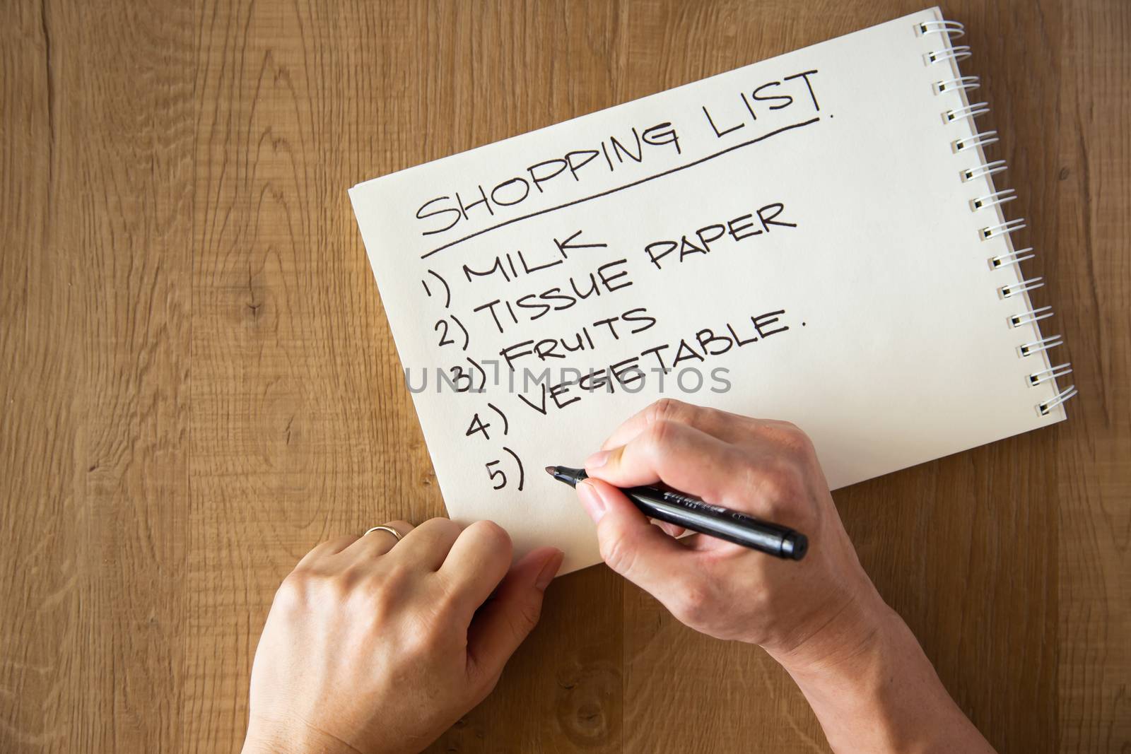 hand writing a shopping list on wooden background