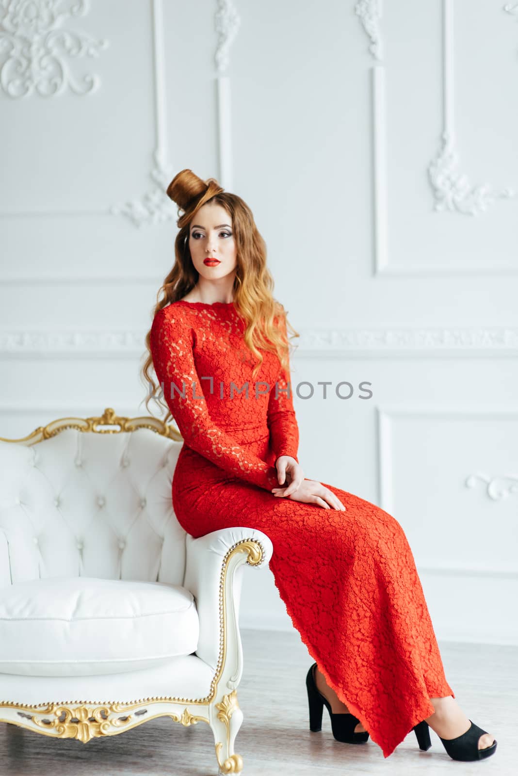 young girl with red hair in a bright red dress in a bright room on an antique sofa