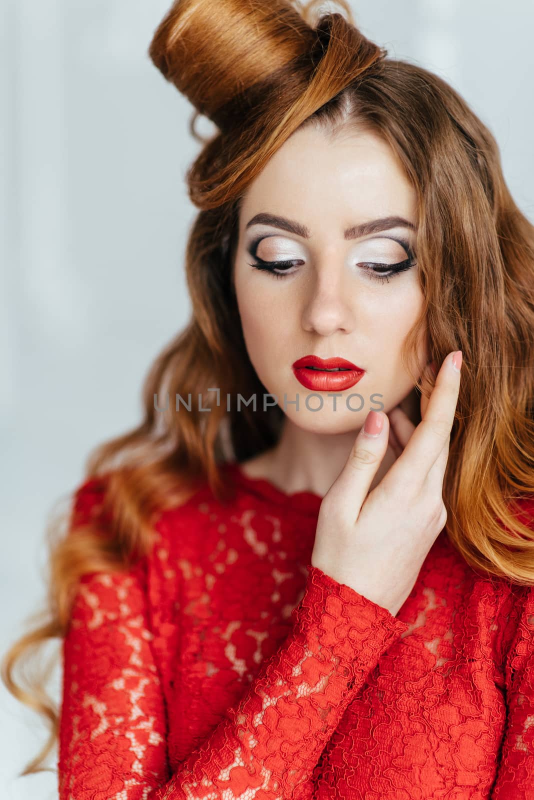 young girl with red hair in a bright red dress in a light room near a white wall