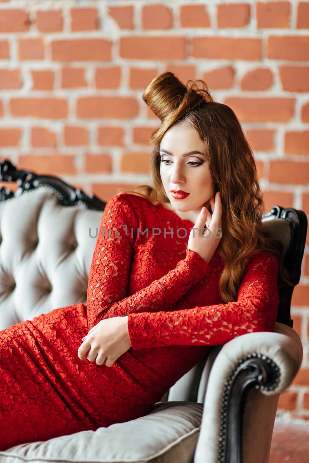 young girl with red hair in a bright red dress in a bright room on an antique sofa