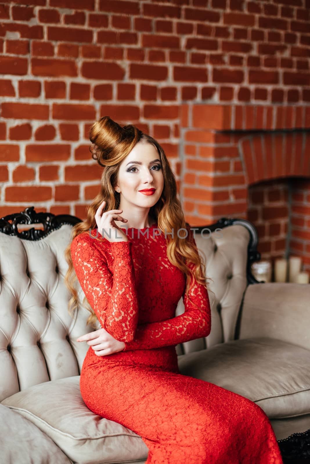 young girl with red hair in a bright red dress in a bright room on an antique sofa