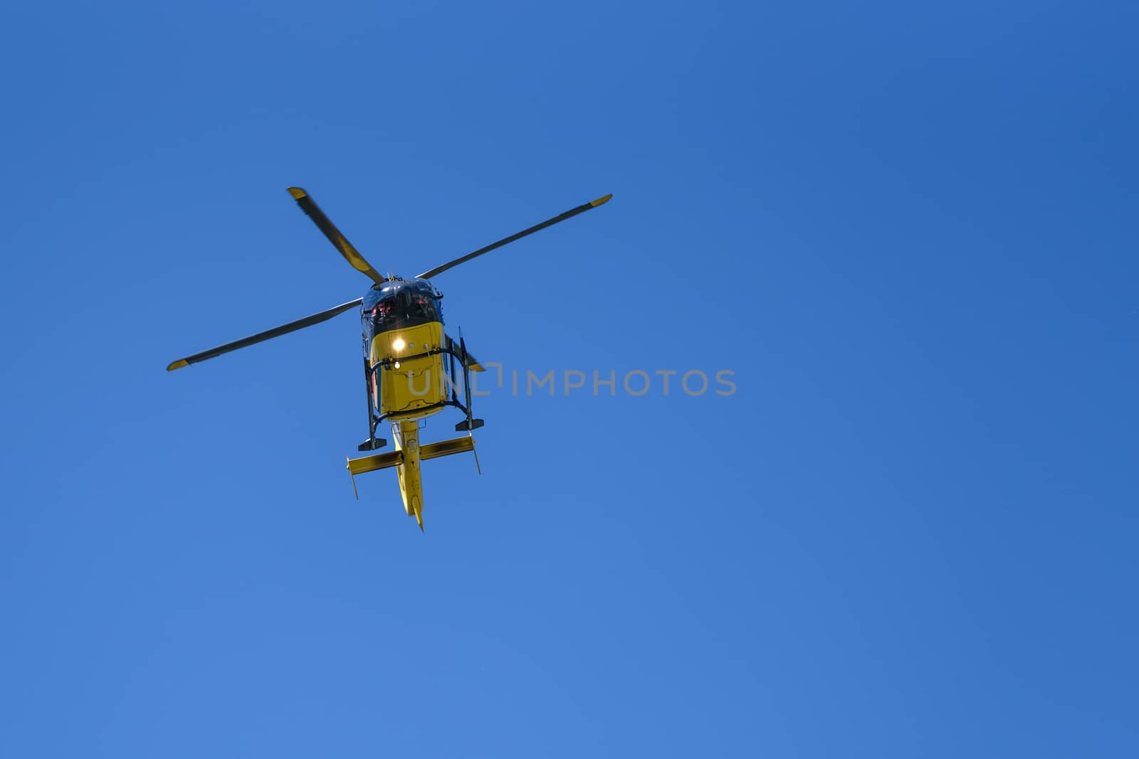 Generic yellow helicopter used for firefighting and rescue operations on the blue sky background - low angel view.