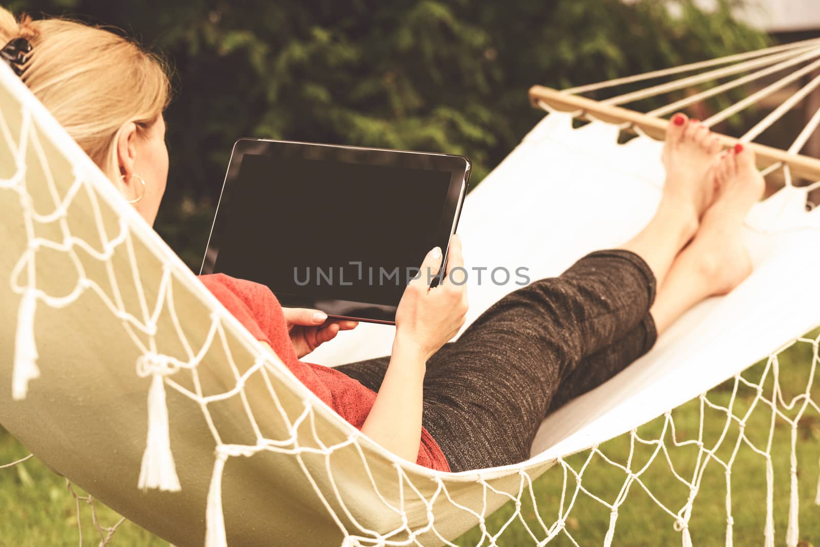 Beautiful woman relaxing on a hammock with and using digital tablet(vintage effect).