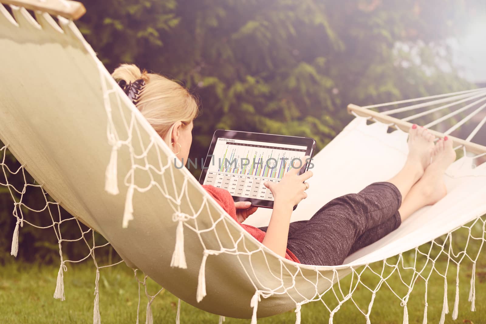 Businesswoman working on a tablet and relaxing in her garden on a hammock (vintage effect)