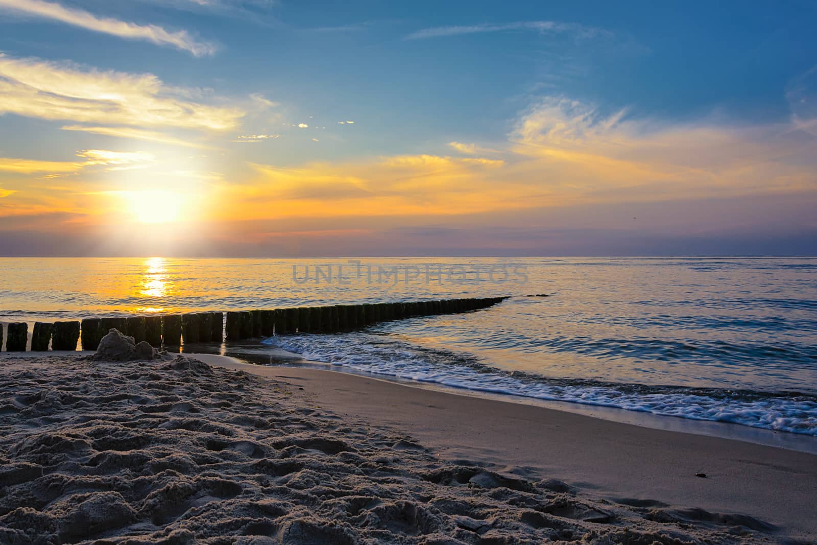Sand on the beach and rippling sea on the background of the picturesque sky at sunset.