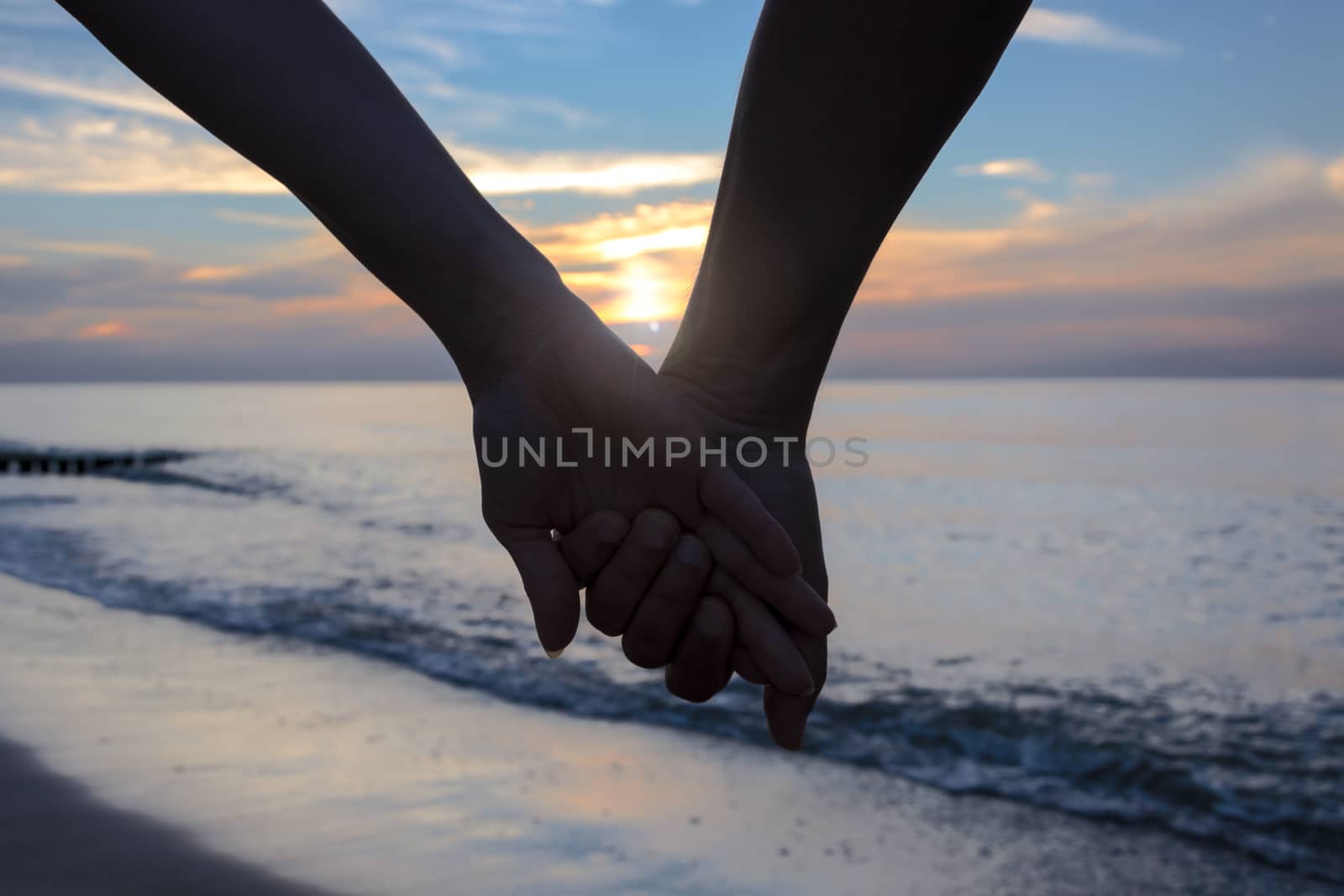 Woman and man in love holding their hands on the beach at sunset.