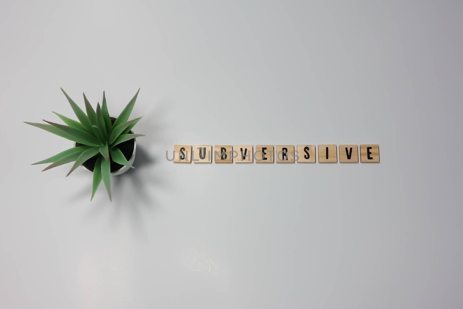 The word Subversive written in wooden letter tiles on a white ba by Jshanebutt