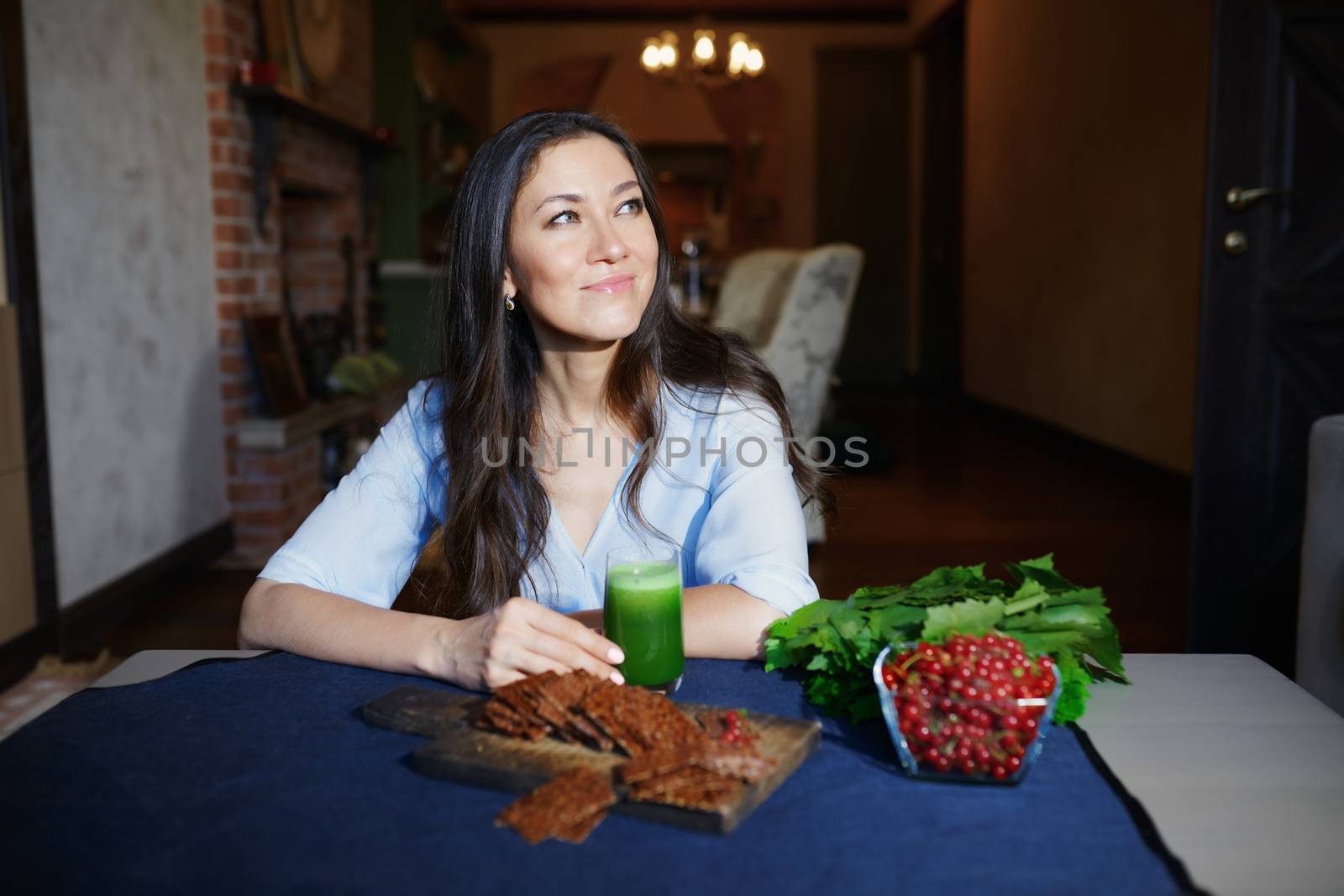 Smiling vegetarian woman sitting at the table with celery fresh juice, flaxseed bread and berries
