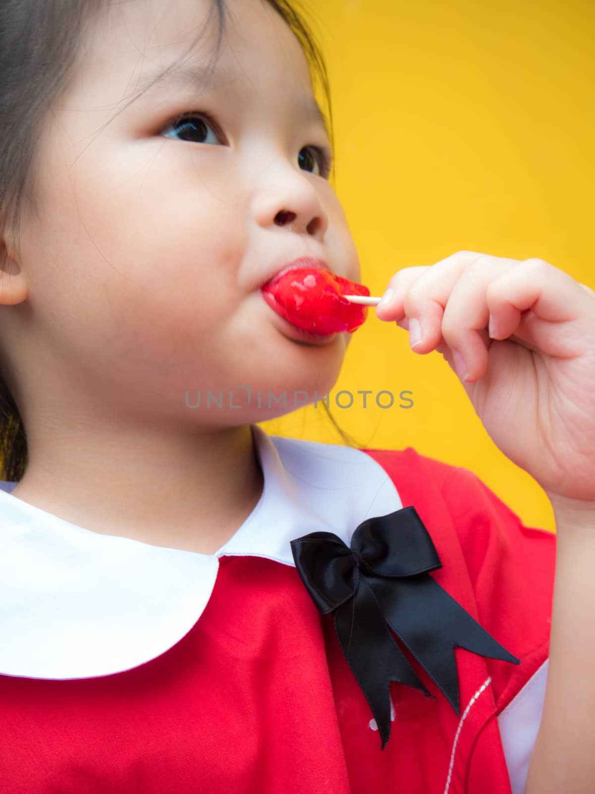 Little girls in red student dressed Eating a red popsicle by Satakorn