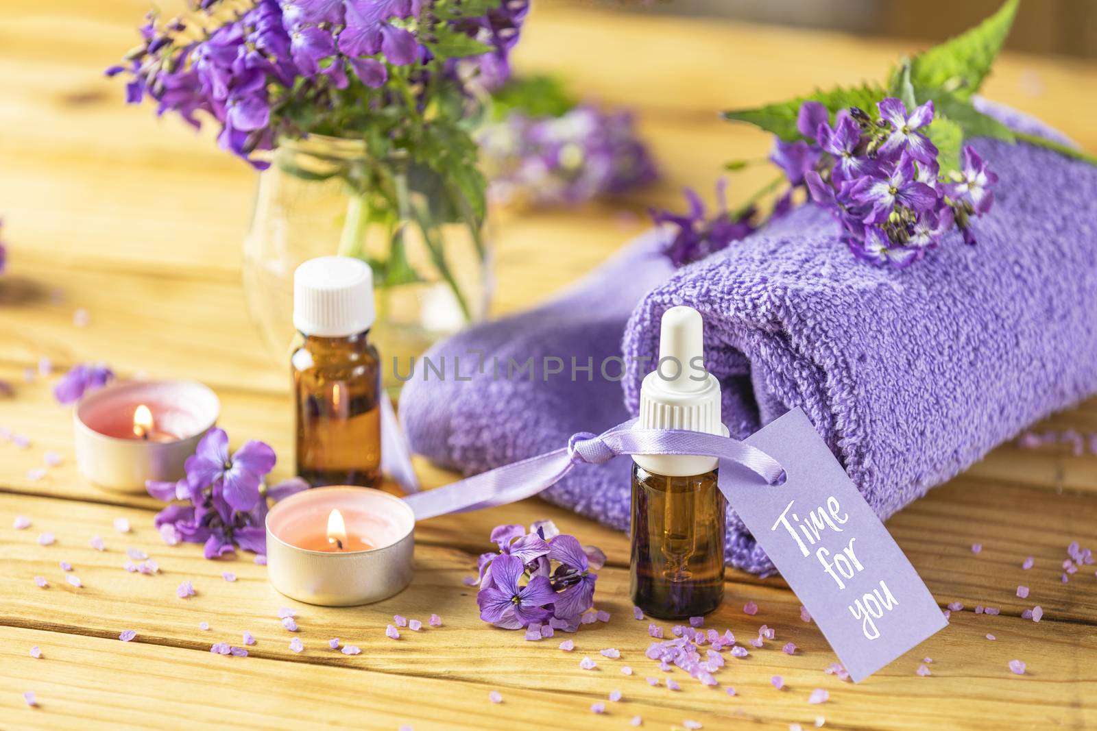 Time for you text phrase on label sticker. Spa still life with violet oil, towel and perfumed candle on natural wood table surface.