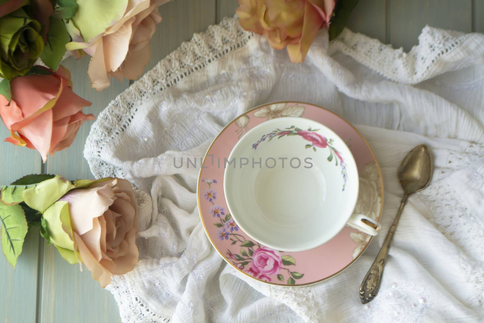 Vintage tea cup with gold rim. White linen tablecloth. Pastel roses, flat lay