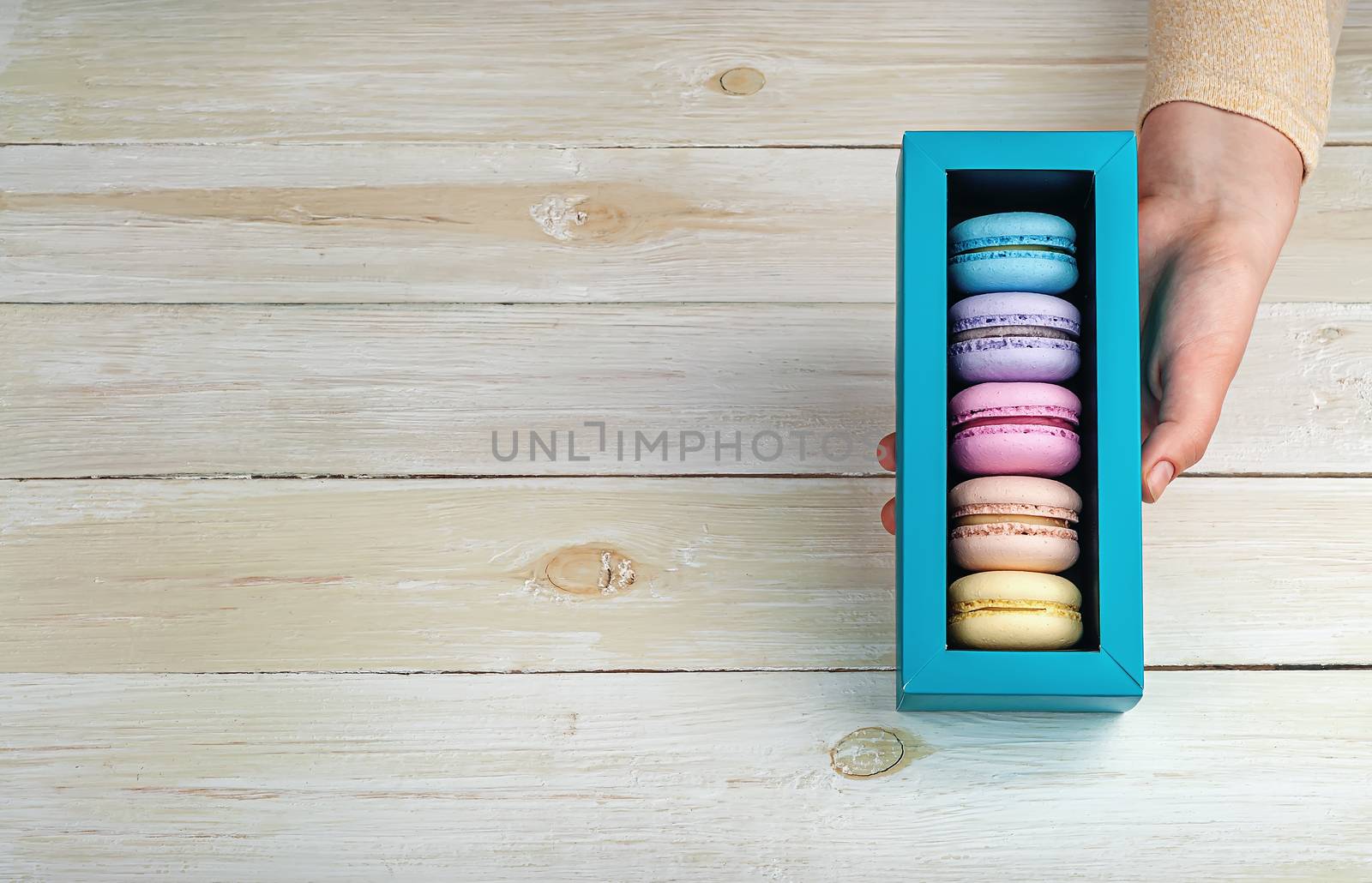 Female hand holds gift box with macaroons on wooden background