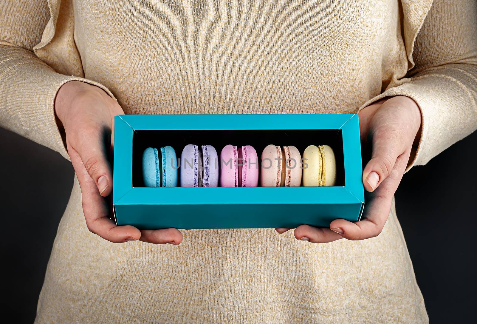 Two beautiful female hands are holding multicolored french macaroons in gift box