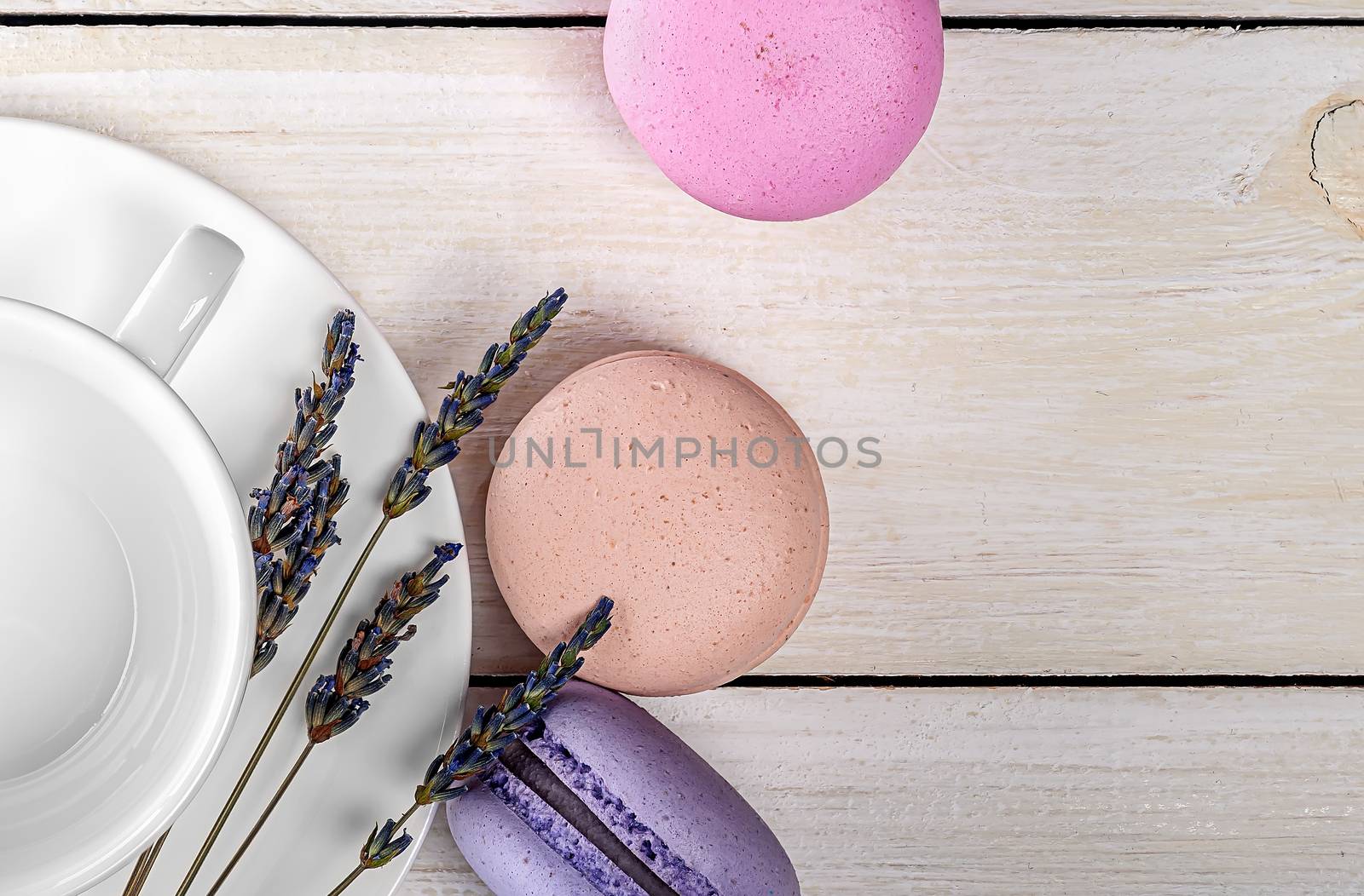 Multicolored macaroons near white coffee cup and lavender closeup top view on wooden table