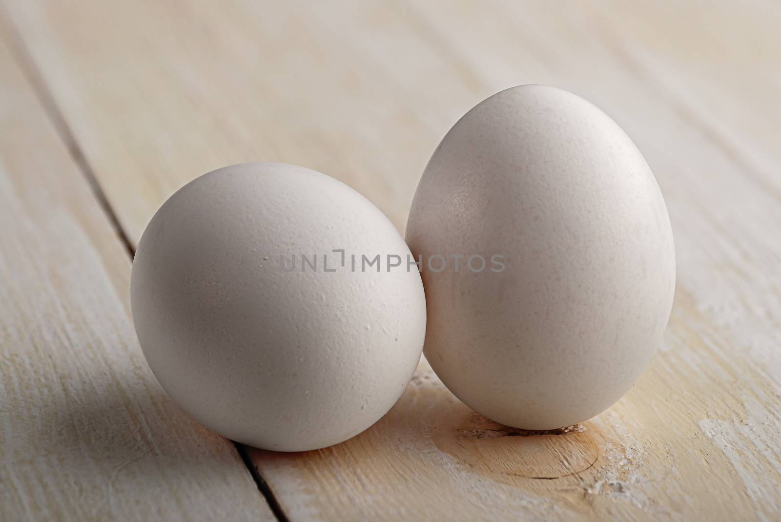 Two white eggs on a white wooden table