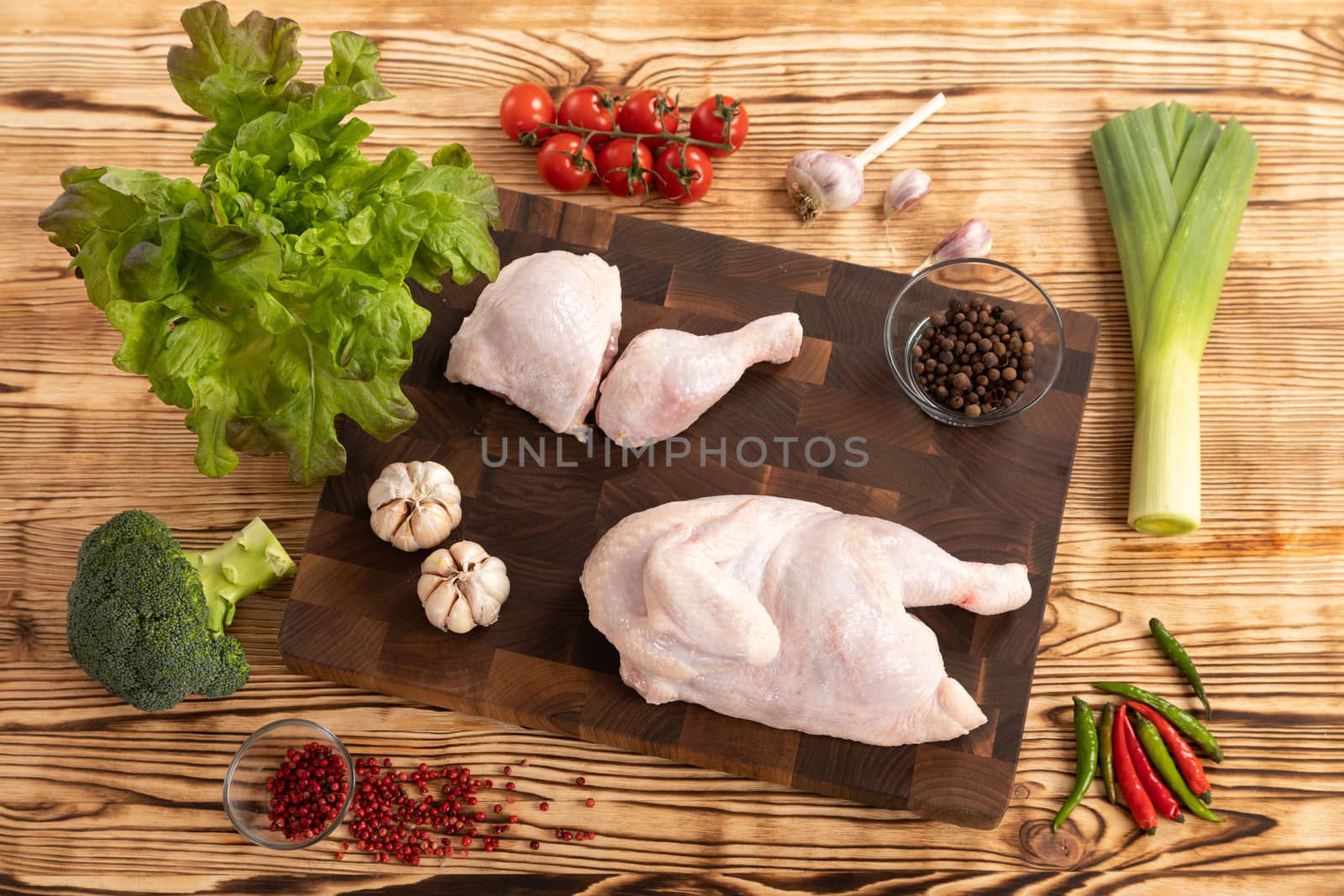 Raw chicken and vegetables for cooking lie on a wooden cutting board