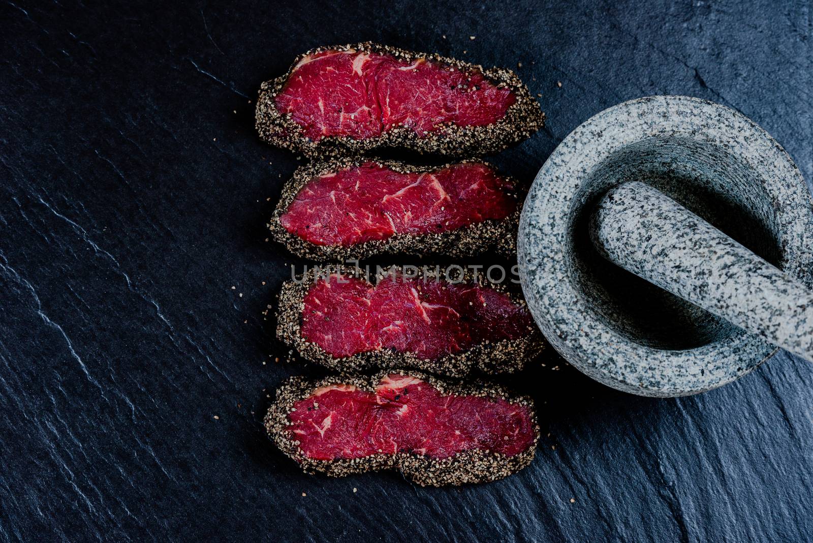 Pepper steaks on stone with mortar bowl and pestle above