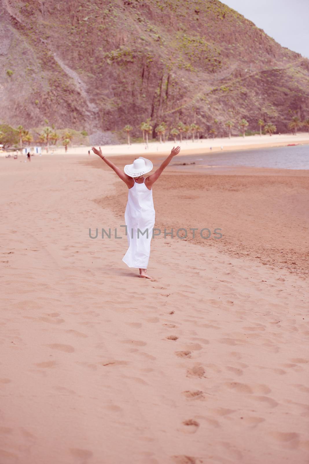 Model in white dress and hat enjoying walk on sandy beach