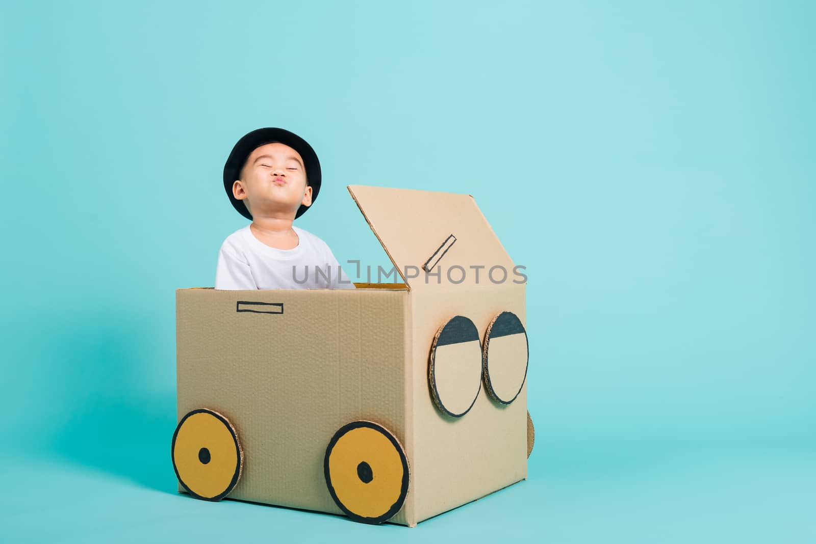 Happy Asian children boy smile in driving play car creative by a cardboard box imagination, summer holiday travel concept, studio shot on blue background with copy space for text