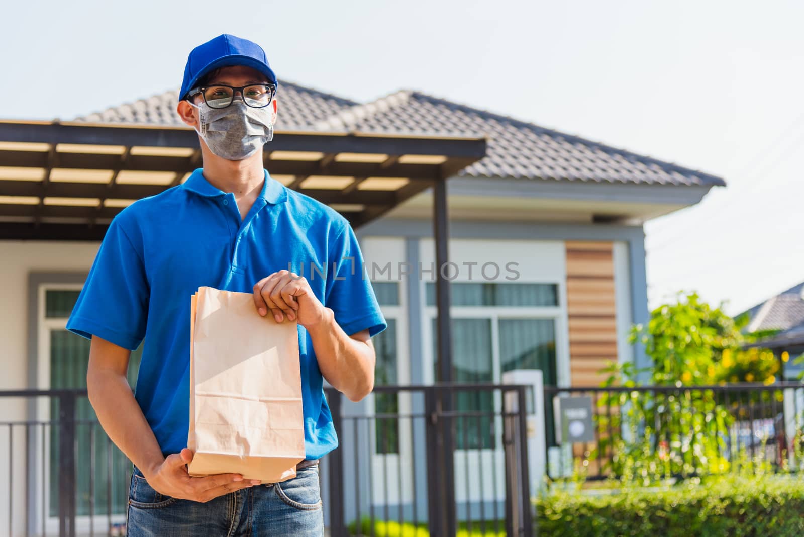 Asian Young delivery man courier online with food order takeaway paper bag containers he protective face mask, service customer in front house under curfew quarantine pandemic coronavirus COVID-19