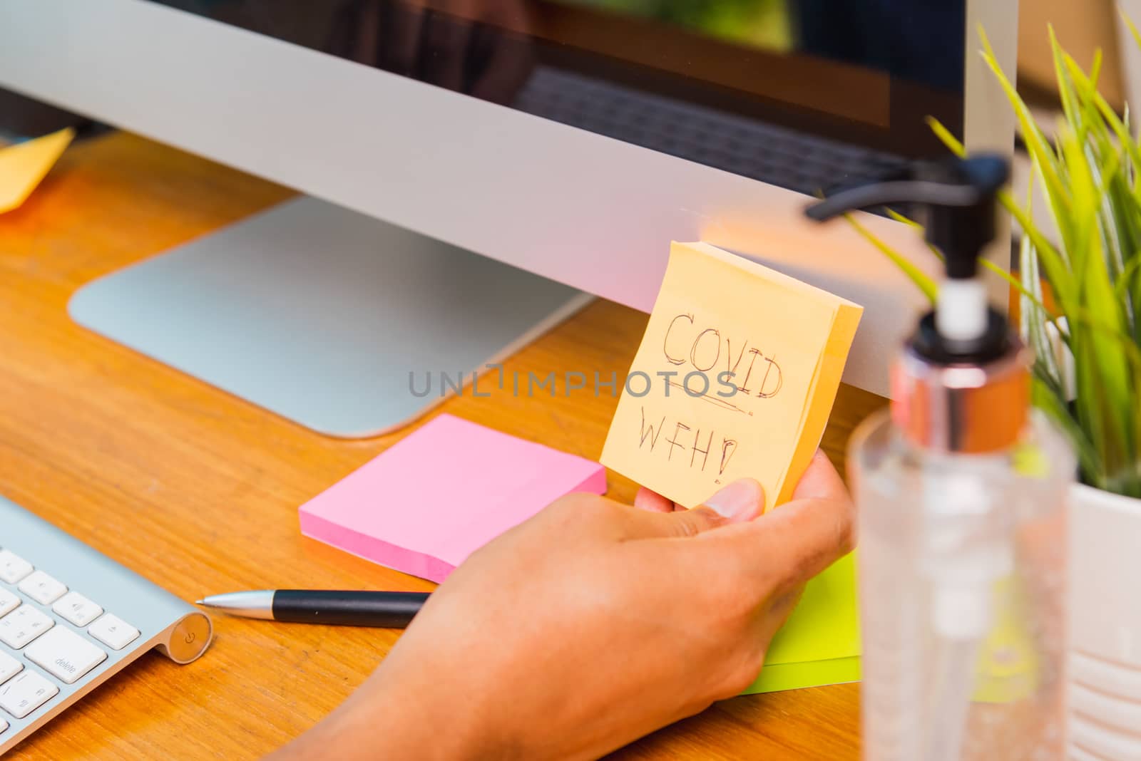 Asian business young man wearing a protective mask with disinfectant gel beside he work from home office with PC computer and he note "COVID WFH" on paper, quarantines disease coronavirus or COVID-19