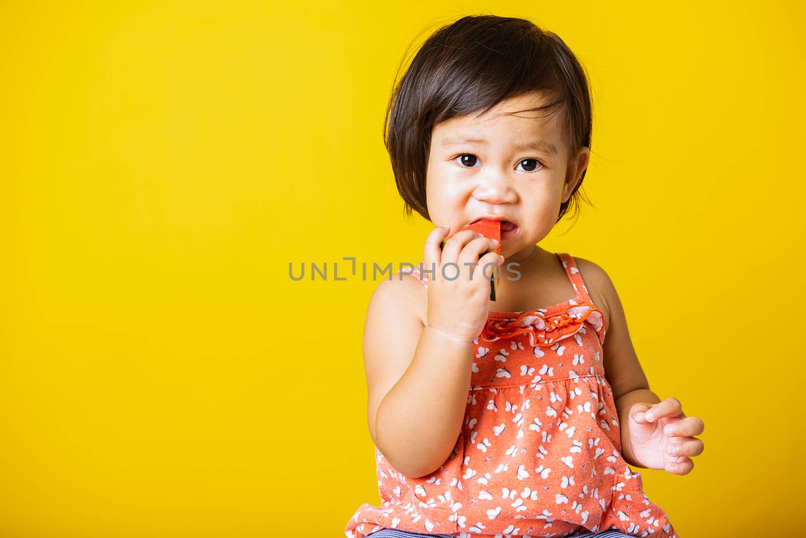 Happy portrait Asian baby or kid cute little girl attractive laugh smile wearing t-shirt playing holds cut watermelon fresh for eating, studio shot isolated on yellow background, healthy food and summer concept