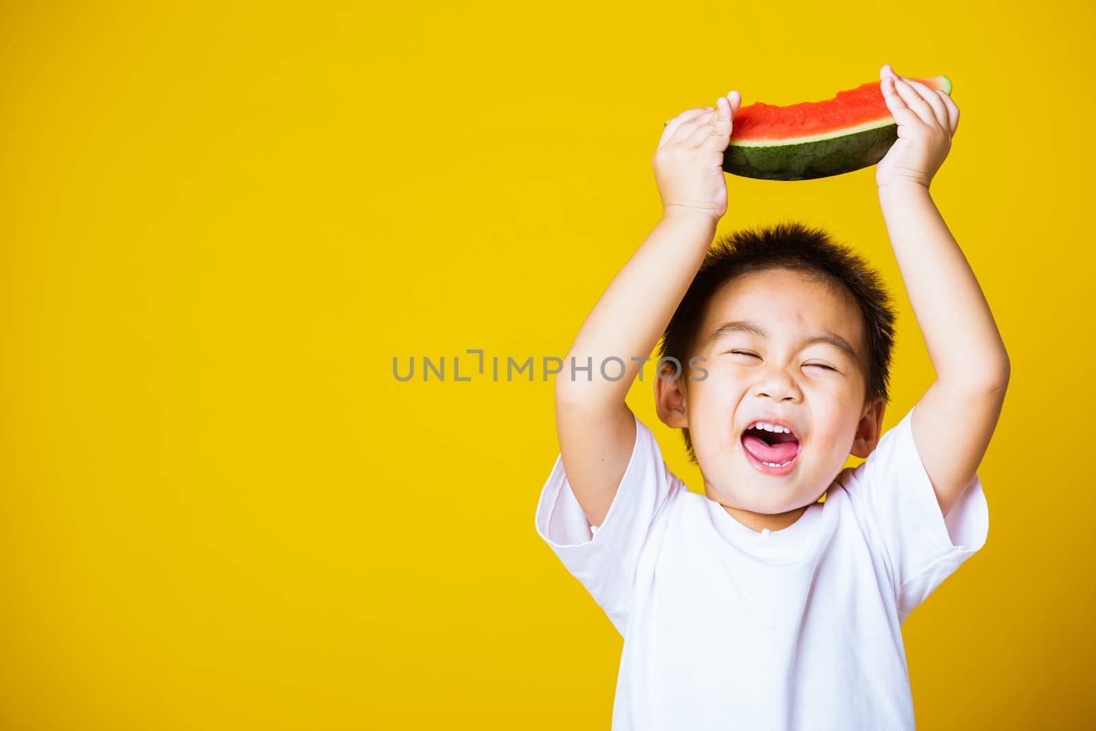 Happy portrait Asian child or kid cute little boy attractive laugh smile playing holds cut watermelon fresh for eating, studio shot isolated on yellow background, healthy food and summer concept