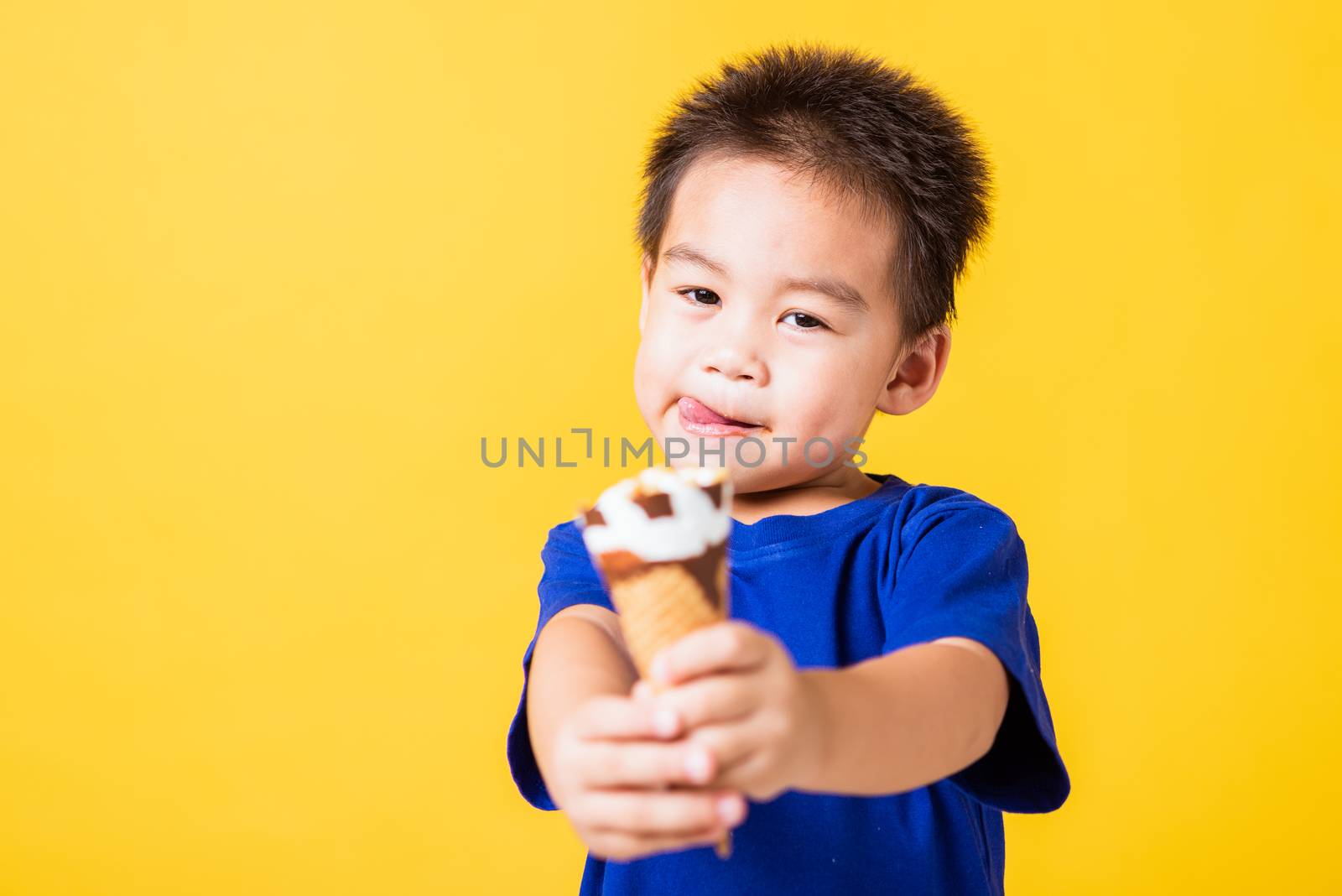 Happy portrait Asian child or kid cute little boy attractive laugh smile playing holds and eating sweet chocolate ice cream waffle cone, studio shot isolated on yellow background, summer concept